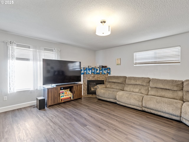 living room with a textured ceiling, baseboards, wood finished floors, and a glass covered fireplace