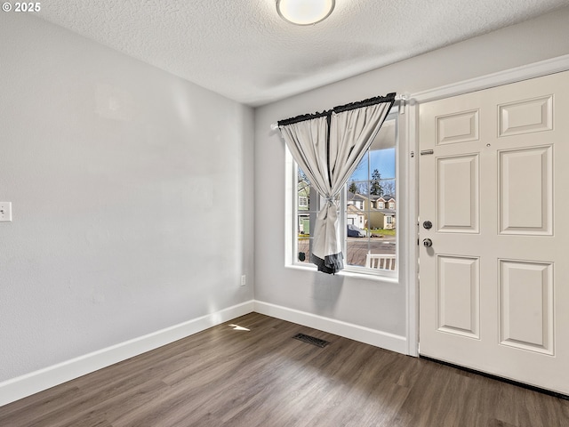 foyer entrance featuring dark wood-style flooring, visible vents, a textured ceiling, and baseboards