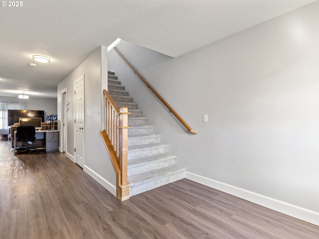 stairs with a textured ceiling, baseboards, and wood finished floors