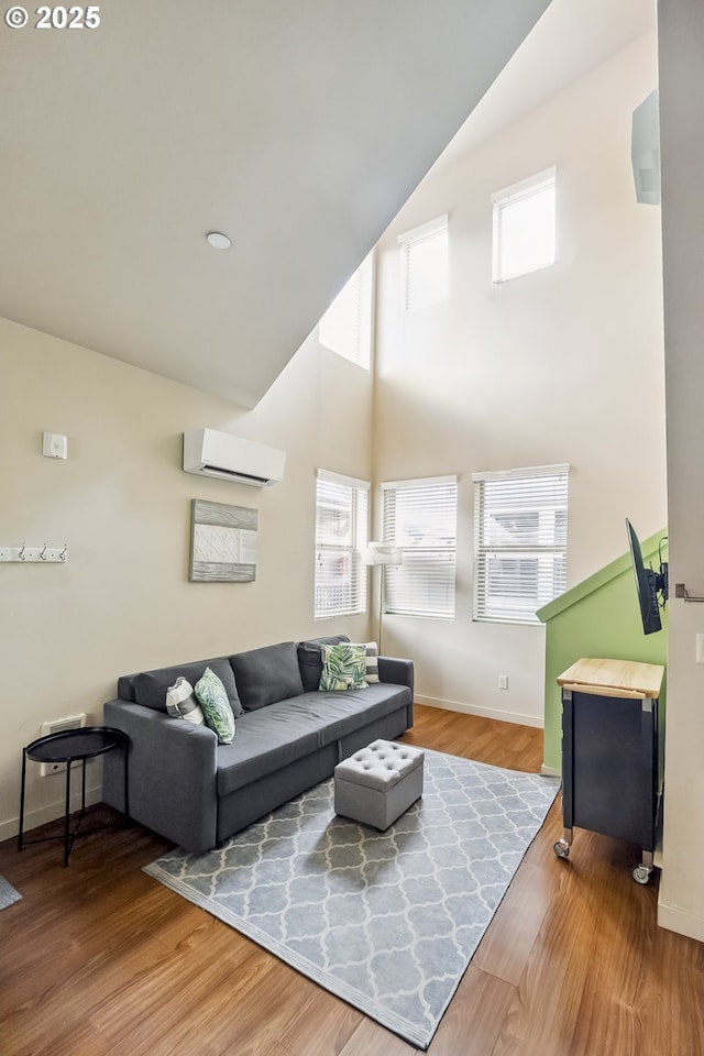 living room featuring baseboards, high vaulted ceiling, an AC wall unit, and wood finished floors