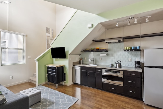 bar featuring backsplash, under cabinet range hood, stairway, stainless steel appliances, and a sink