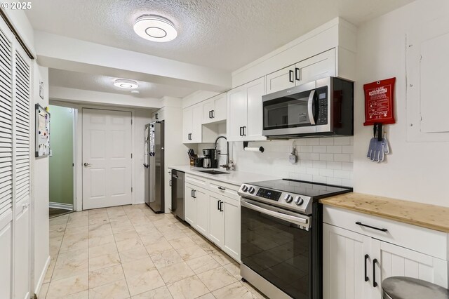 16500 SW Satterberg Rd, Beaverton, OR 97007 - kitchen with stainless steel appliances, a sink, light marble finish flooring, white cabinets, and a textured ceiling