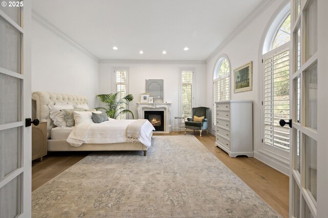 bedroom featuring a glass covered fireplace, baseboards, recessed lighting, crown molding, and wood finished floors