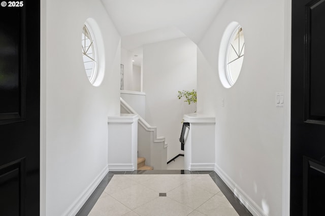 foyer featuring baseboards, dark tile patterned floors, stairs, and a healthy amount of sunlight