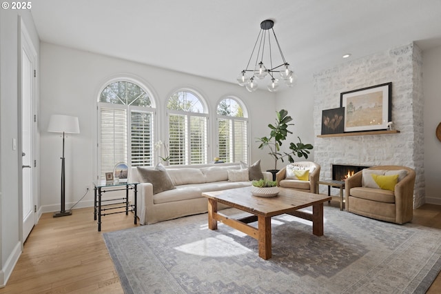 living area featuring light wood-style flooring, a notable chandelier, baseboards, and a stone fireplace