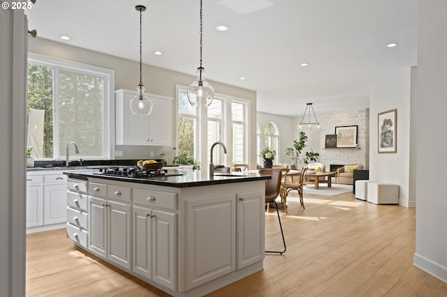 kitchen with a kitchen island with sink, a sink, dark countertops, white cabinetry, and a fireplace