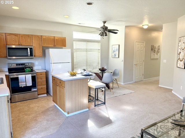 kitchen with stainless steel appliances, a kitchen island, a breakfast bar area, ceiling fan, and light carpet