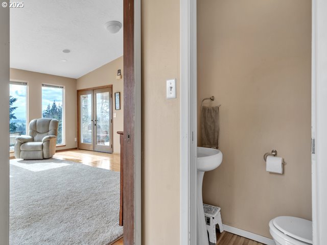 half bathroom featuring lofted ceiling, toilet, wood finished floors, baseboards, and french doors