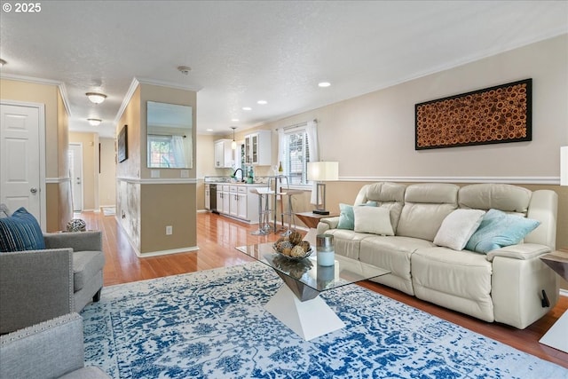 living room with light wood-style floors, a textured ceiling, crown molding, and recessed lighting