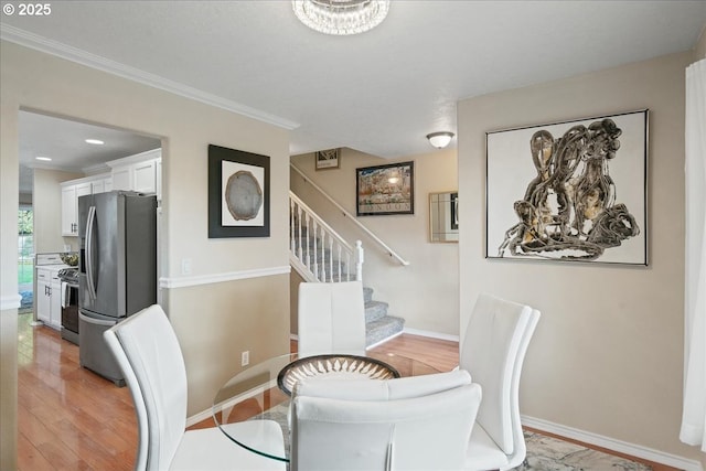 dining area featuring light wood-style floors, ornamental molding, baseboards, and stairs