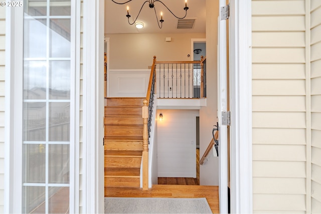 staircase featuring an inviting chandelier, visible vents, and wood finished floors