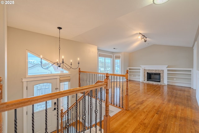 hall featuring lofted ceiling, built in shelves, an upstairs landing, light wood finished floors, and an inviting chandelier