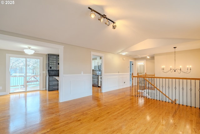 spare room featuring wainscoting, lofted ceiling, light wood-type flooring, a chandelier, and track lighting