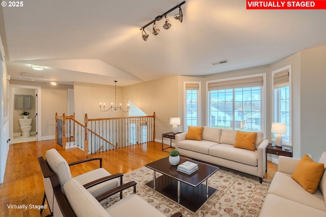 living area featuring visible vents, an inviting chandelier, vaulted ceiling, wood finished floors, and baseboards