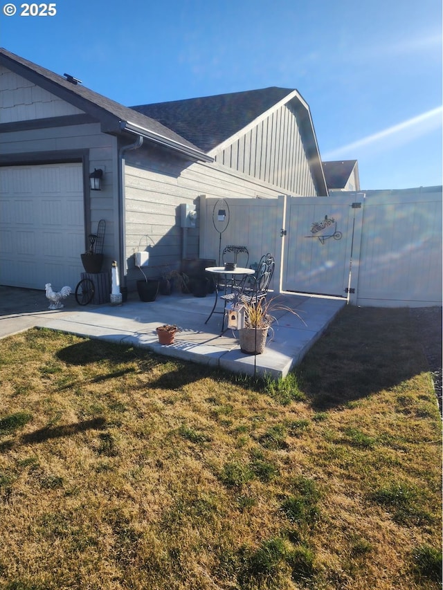 exterior space featuring an attached garage, a gate, fence, and a lawn