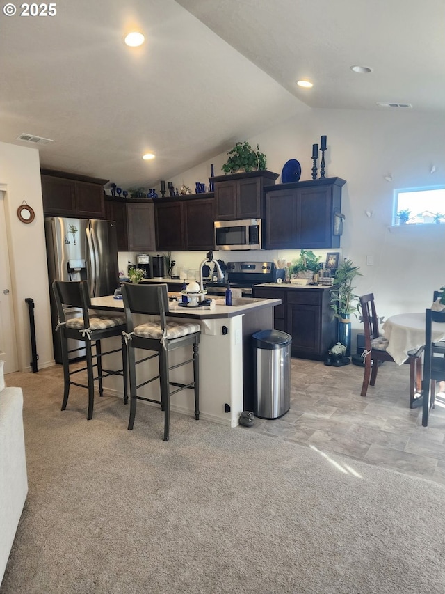 kitchen with a breakfast bar, stainless steel appliances, lofted ceiling, visible vents, and a kitchen island with sink