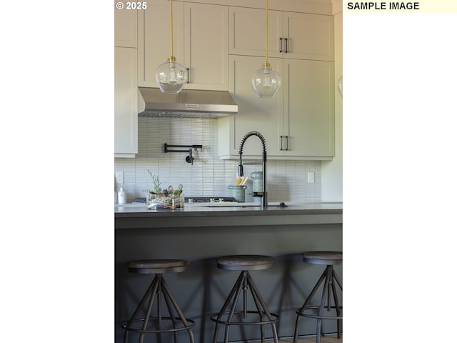 kitchen with a sink, tasteful backsplash, a kitchen bar, and under cabinet range hood