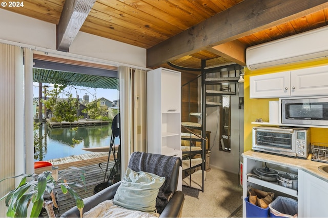 kitchen with stainless steel microwave, beamed ceiling, an AC wall unit, carpet floors, and white cabinetry