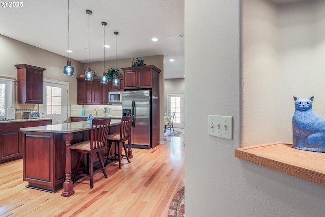 kitchen featuring appliances with stainless steel finishes, a kitchen island, decorative backsplash, light hardwood / wood-style flooring, and a breakfast bar area