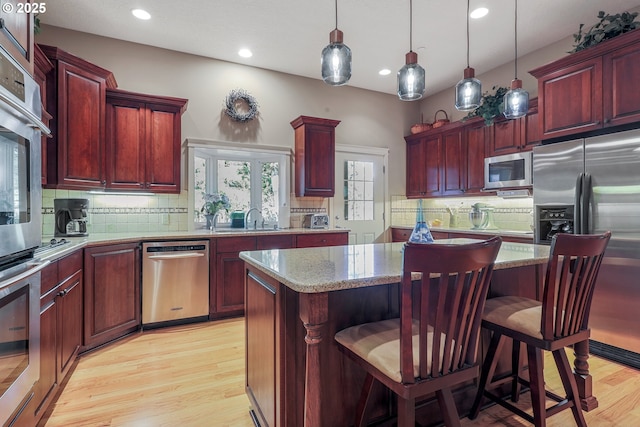 kitchen featuring light hardwood / wood-style flooring, hanging light fixtures, appliances with stainless steel finishes, a breakfast bar, and a kitchen island