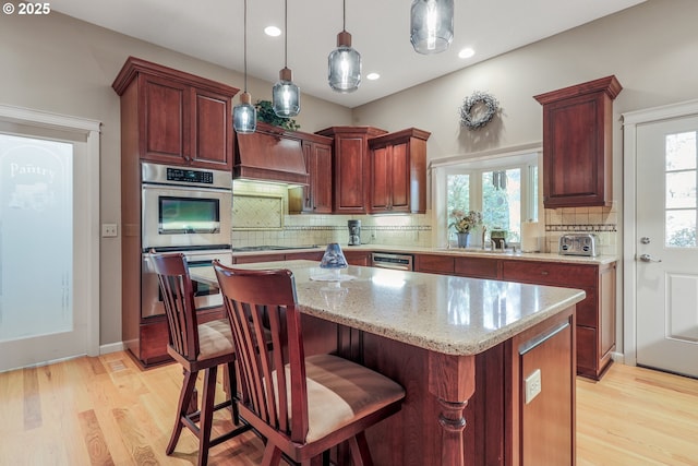 kitchen featuring a center island, light hardwood / wood-style floors, light stone countertops, stainless steel double oven, and pendant lighting