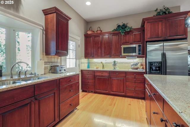 kitchen featuring light stone countertops, stainless steel appliances, tasteful backsplash, sink, and light hardwood / wood-style flooring