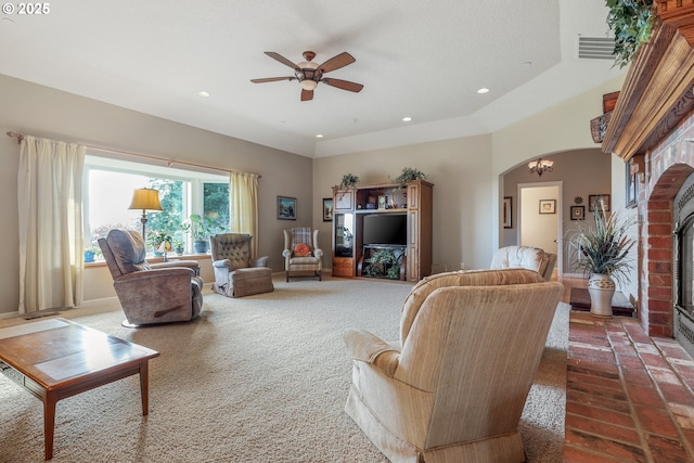 living room featuring a brick fireplace, dark carpet, and ceiling fan