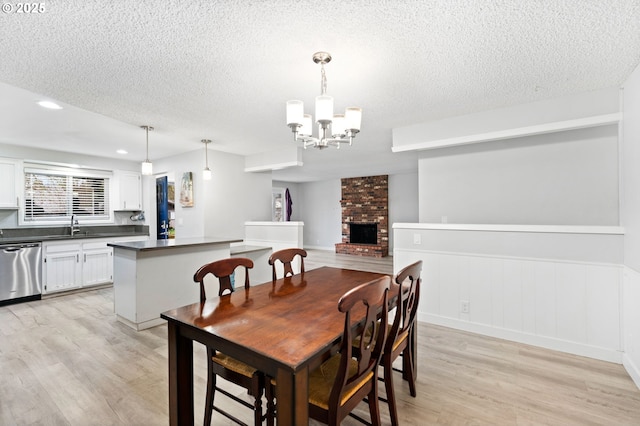 dining room featuring a chandelier, light wood-type flooring, a brick fireplace, and a textured ceiling