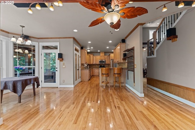 7444 SE 114th Ave, Portland, OR 97266 - kitchen featuring crown molding, stainless steel microwave, ceiling fan, a breakfast bar area, and light wood finished floors