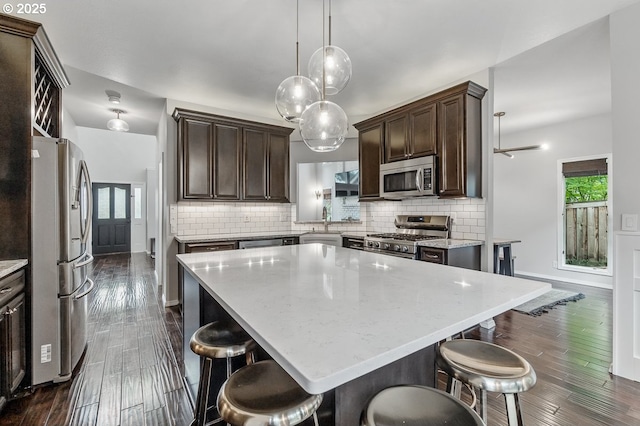 11255 SW Chickadee Ter, Beaverton, OR 97007 - kitchen with appliances with stainless steel finishes, dark brown cabinetry, dark wood-style flooring, decorative backsplash, and a kitchen island