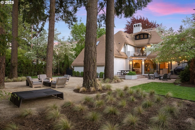 back house at dusk featuring a patio area, an outdoor living space with a fire pit, and a balcony