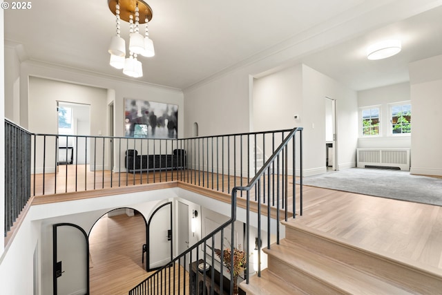 stairs with ornamental molding, hardwood / wood-style floors, a chandelier, and radiator heating unit