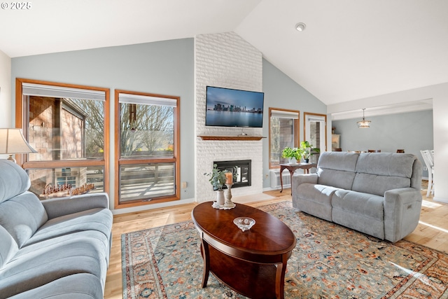 living room with vaulted ceiling, a brick fireplace, and light wood-type flooring