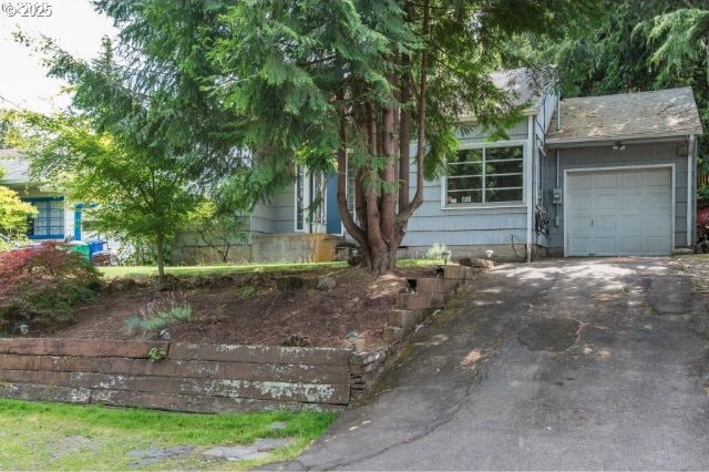 view of property hidden behind natural elements with aphalt driveway and a garage