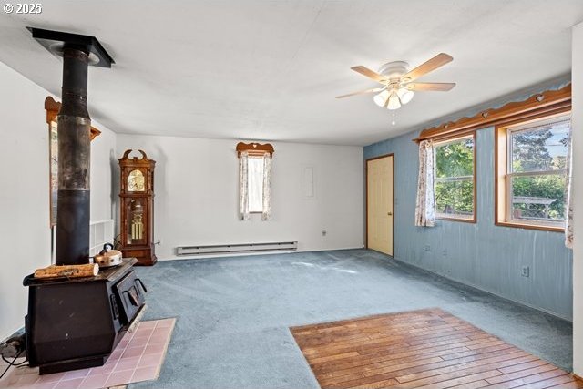 387 E Linden Way, Heppner, OR 97836 - unfurnished living room featuring a wood stove, a baseboard heating unit, a ceiling fan, and carpet