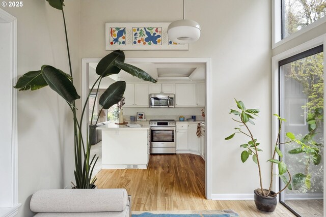 kitchen featuring light countertops, stainless steel appliances, white cabinetry, light wood-style floors, and hanging light fixtures