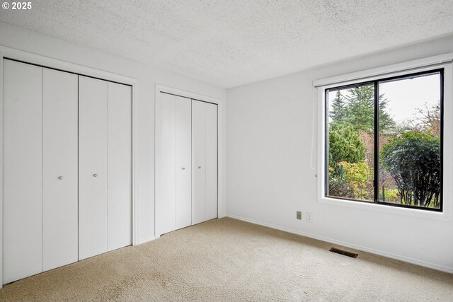 unfurnished bedroom featuring visible vents, multiple closets, carpet flooring, and a textured ceiling