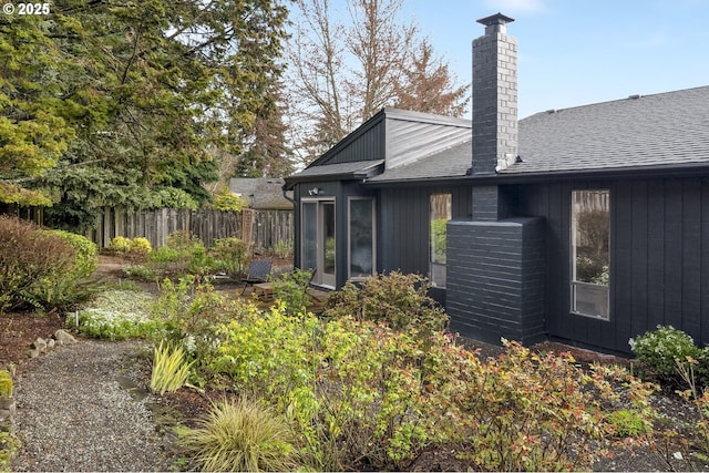 rear view of house with a chimney, a shingled roof, and fence