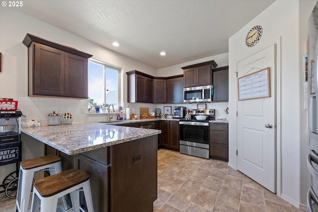 3 Patty Cir, Milton-Freewater, OR 97862 - kitchen featuring appliances with stainless steel finishes, dark brown cabinetry, a peninsula, light stone countertops, and recessed lighting