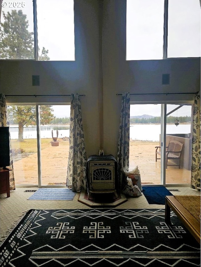 living room featuring a high ceiling, a healthy amount of sunlight, a water view, and a wood stove