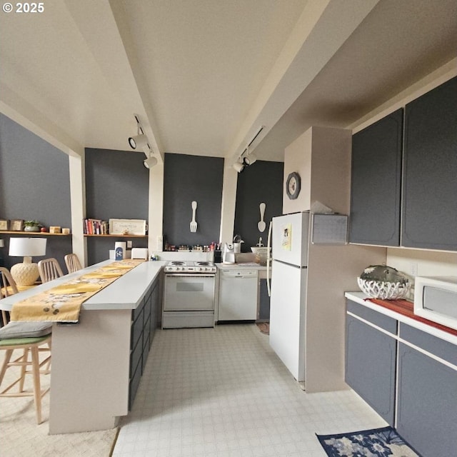 kitchen featuring white appliances, a breakfast bar area, rail lighting, and kitchen peninsula