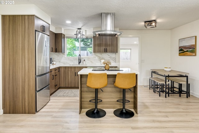 3711 N Alaska Pl, Portland, OR 97217 - kitchen featuring stainless steel fridge, island range hood, a kitchen breakfast bar, a sink, and light wood-style flooring