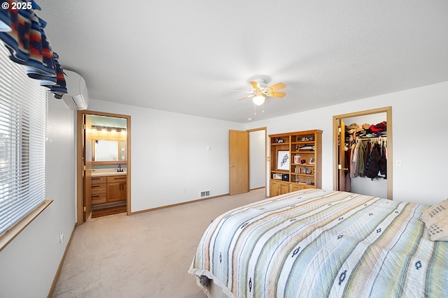 carpeted bedroom featuring a wall mounted air conditioner, a walk in closet, ceiling fan, ensuite bath, and a closet