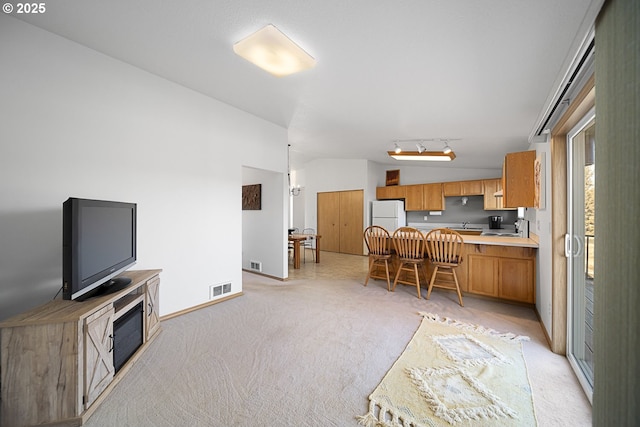 kitchen featuring lofted ceiling, kitchen peninsula, light carpet, and white fridge