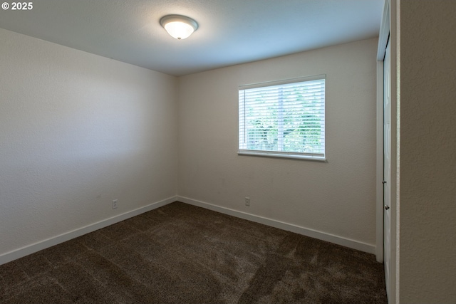 empty room with dark colored carpet and baseboards