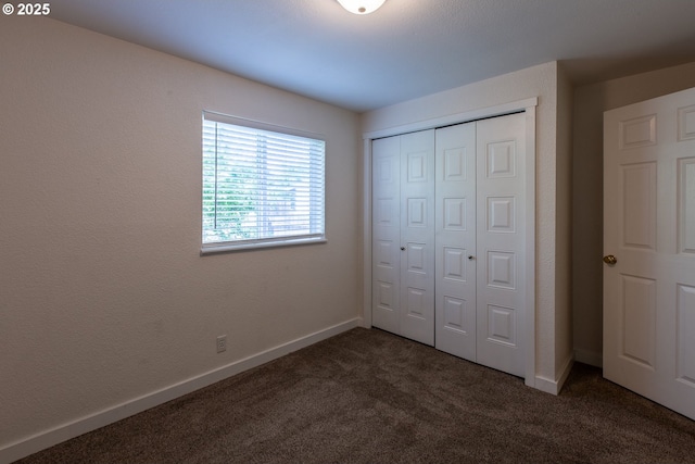 unfurnished bedroom featuring dark colored carpet, a closet, and baseboards