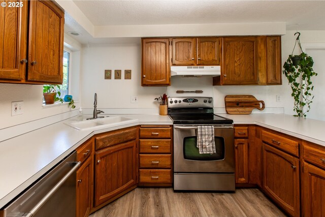 kitchen with stainless steel appliances, under cabinet range hood, a sink, light wood-type flooring, and light countertops
