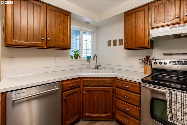 kitchen featuring stainless steel appliances, under cabinet range hood, a sink, light countertops, and brown cabinets