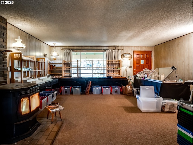 interior space with a wood stove, wood walls, a textured ceiling, and carpet flooring