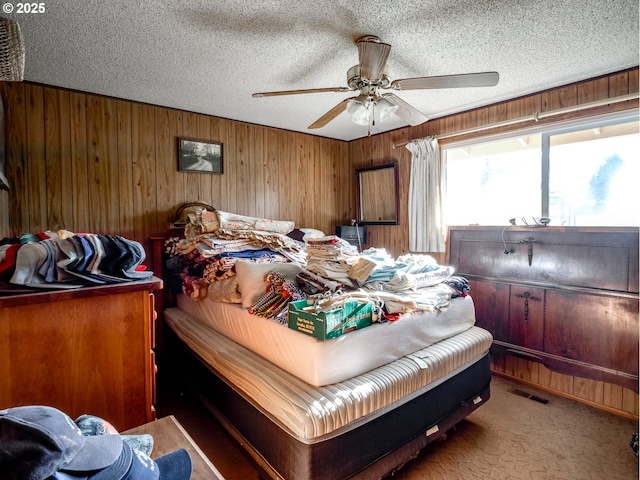 bedroom with ceiling fan, carpet, wooden walls, and a textured ceiling